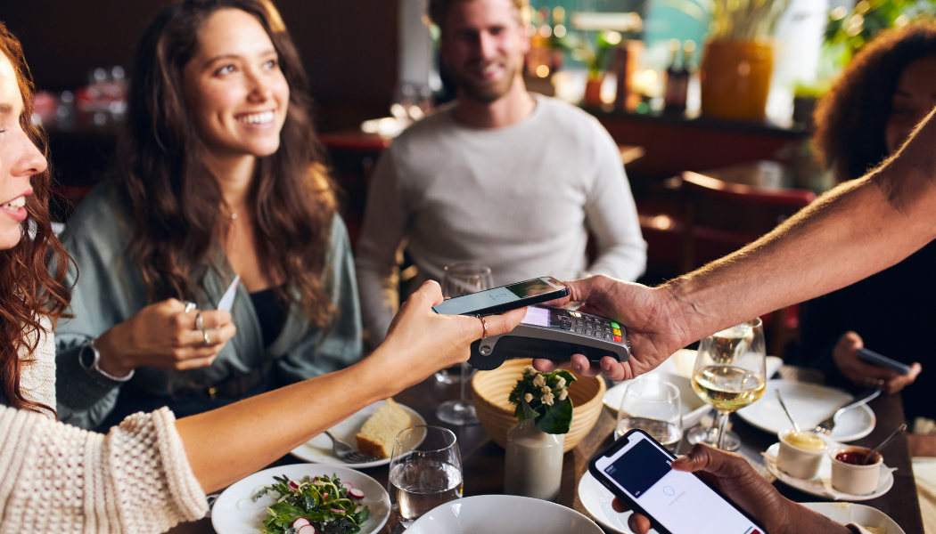 Groupe d'amis au restaurant réglant l'addition sur un terminal de paiement